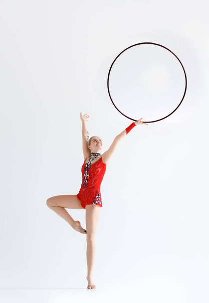 Urheilukilpailu. Naisten voimistelija punaisessa trikoissa harjoittelemassa hula-vanteella, eristetty valkoisella
 - Valokuva, kuva