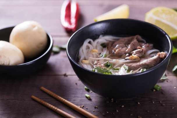 Asian cuisine, Vietnamese pho bo soup in a black plate on a wooden background - Fotografie, Obrázek