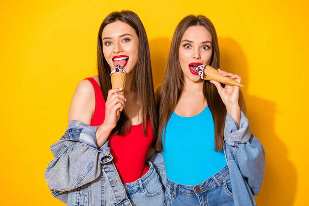 Portrait of positive cheerful charming girls youngsters eat delicious icecream scoops waffle cone wear bright red singlet isolated over shine color background - 写真・画像