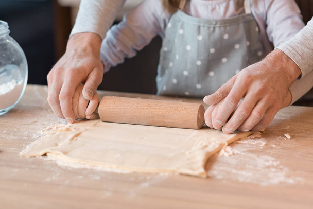 Father Helping To Little Daughter Roll The Dough On Kitchen Table - Photo, Image