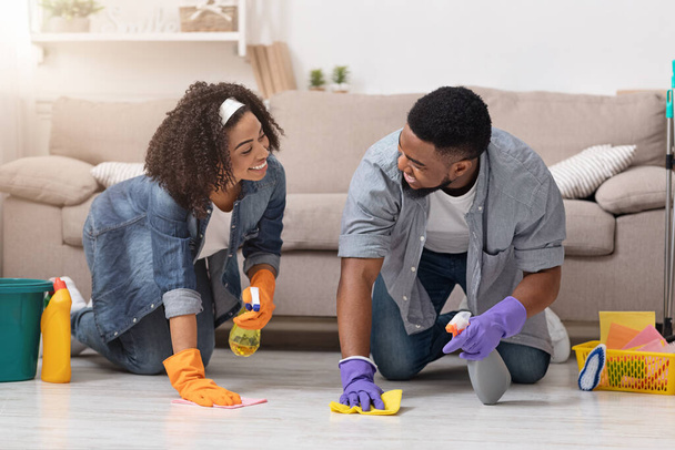 Концепция домашнего хозяйства. Молодая черная пара проводит весеннюю уборку в своей квартире вместе
 - Фото, изображение