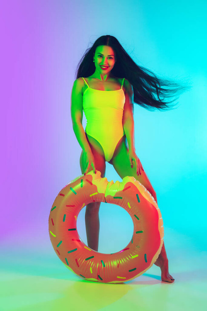 Beautiful girl in fashionable swimsuit isolated on gradient studio background in neon light. Summer, resort, fashion and weekend concept - Foto, Imagem
