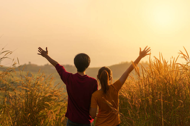 Asian woman and man standing and hand up in meadow and looking far away at sunrise time. - Foto, immagini
