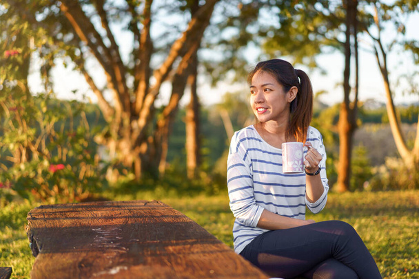 Mujer asiática sonrisa y beber taza de café en el jardín por la mañana
. - Foto, Imagen