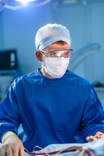Portrait of male surgeon in operation theater. Doctor in scrubs and medical mask in modern hospital operating room. - 写真・画像