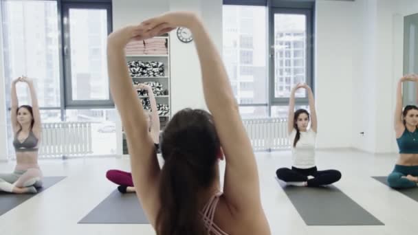 A fiatal női jógaoktató egyensúlyt mutat, pózol és beszél a diákokkal, míg más nők csendben ismétlik a testtartást. Csoportos gyakorlat. - Felvétel, videó