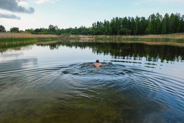  Muž plave v opuštěném jezeře před deštěm na Ukrajině. Kruhy na vodě. Kopírovat prostor. - Fotografie, Obrázek