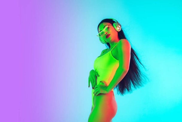 Beautiful girl in fashionable swimsuit isolated on gradient studio background in neon light. Summer, resort, fashion and weekend concept - Φωτογραφία, εικόνα