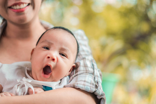 Joven mujer asiática sosteniendo a un bebé recién nacido en sus brazos, bostezando bebé, enfoque selectivo
. - Foto, Imagen