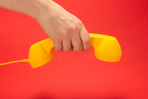 Yellow handset on a red background in woman hand. Copy space. - Photo, Image
