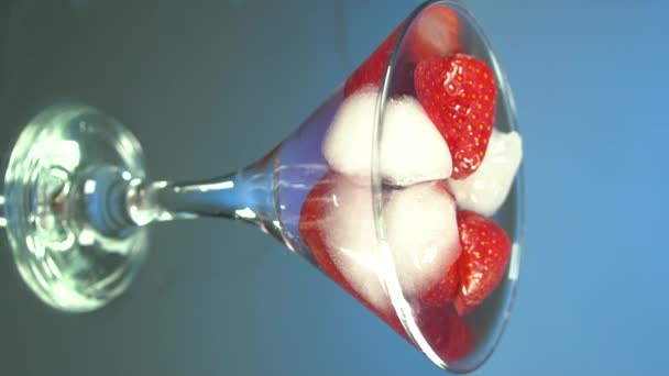 Pouring tequila into glass of ice cubes and strawberries, slow motion, mirror background. Vertical video for smartphones and tablets - Footage, Video