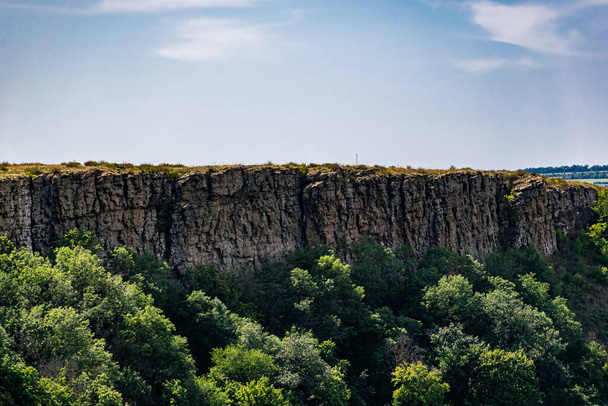 An unusual view in the Rostov region of the stony Zaitsev rocks, around green deciduous trees, dry yellow grass, blue sky and Sunny warm summer light - 写真・画像