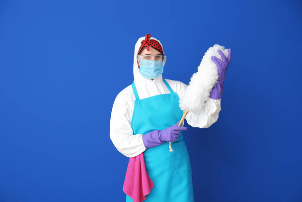 Housewife in protective costume and with dust brush on color background - Photo, Image