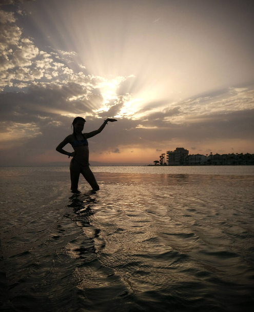 Krásný západ slunce s mraky a zapadající slunce a silueta dívky stojící v moři - Fotografie, Obrázek