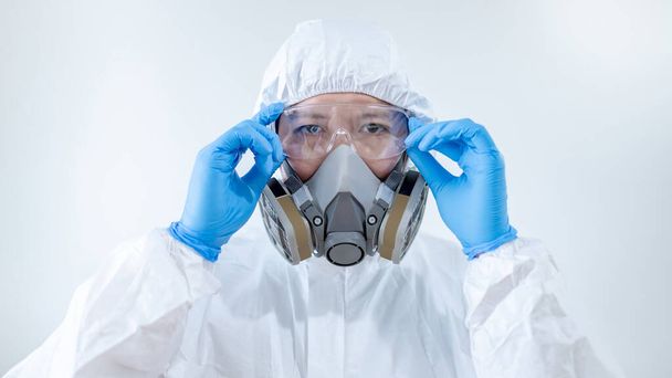 Tiedemies tai virologi mies yllään biovaara kemiallinen suojapuku, suojalasit ja naamio. Mieslääkäri tai lääkintätyöntekijä, jolla on henkilönsuojain ja kumihanskat Coronavirus (COVID-19) infektion ehkäisemiseksi
. - Valokuva, kuva