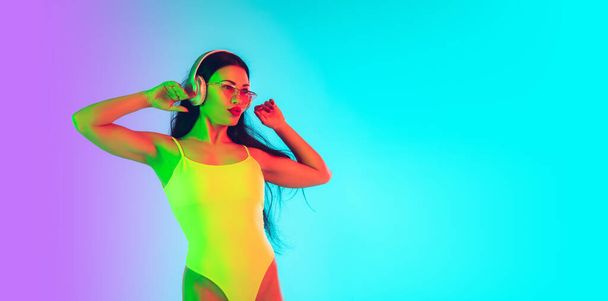 Beautiful girl in fashionable swimsuit isolated on gradient studio background in neon light. Summer, resort, fashion and weekend concept. Flyer with copyspace. - Foto, immagini