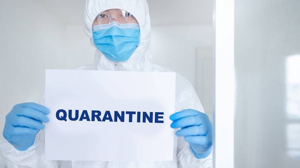 Doctor or medical worker in personal protective equipment (PPE) suit, mask and gloves showing paper with message Quarantine. Quarantine campaign during Coronavirus (COVID-19) pandemic - Foto, Bild