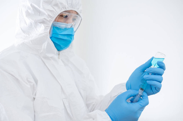 Koncept očkování COVID-19. Lékař nebo lékař v obleku osobních ochranných prostředků (PPE) s maskou, brýlemi a gumovými rukavicemi, které drží injekční stříkačku a injekční lahvičku s lékem na injekci koronaviru. - Fotografie, Obrázek