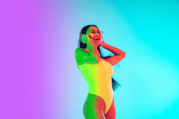 Beautiful girl in fashionable swimsuit isolated on gradient studio background in neon light. Summer, resort, fashion and weekend concept - Photo, Image