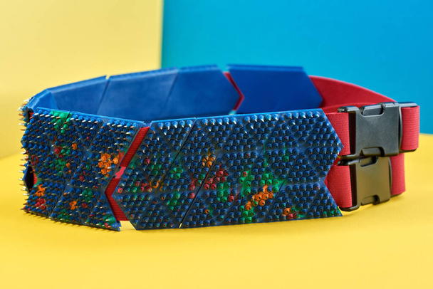 Massage du dos sous la forme d'une ceinture orange-bleue avec des pointes, des aiguilles en métal, se trouvent sur le ruban vert sur fond jaune-bleu. Tournage thématique et thématique. relaxation et santé
 - Photo, image