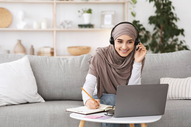 笑顔アラビア語の女の子でスカーフとヘッドセット自宅でノートパソコンで勉強 - 写真・画像