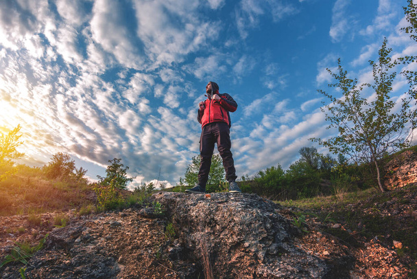 чоловік з рюкзаком на спині стоїть на краю скелі і дивиться на захід сонця
 - Фото, зображення