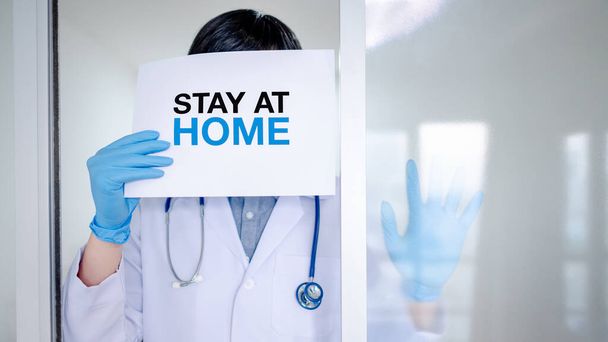 Orvos vagy egészségügyi dolgozó egyéni védőfelszerelésben (PPE), maszk és kesztyű papírral és üzenettel Maradjon otthon. Karanténkampány a Coronavirus (COVID-19) világjárvány idején. - Fotó, kép