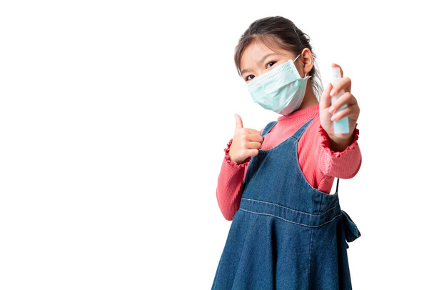 Asian girl wearing medical protective face mask for protect infection the virus and show thumbs up sign and hold alcohol spray bottle isolated on white background, With clipping path. - Foto, Bild
