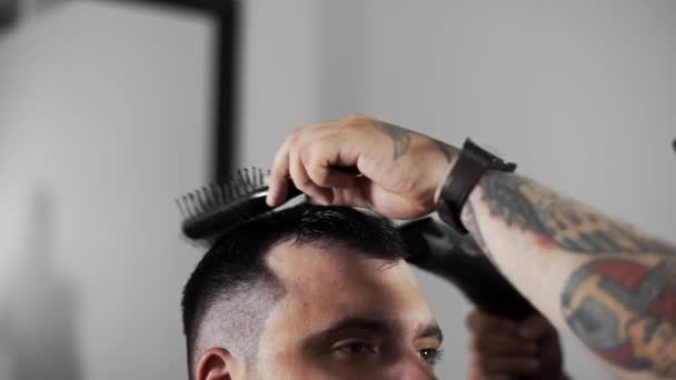 barber dries hair and makes hair styling for customer at barber shop - Metraje, vídeo
