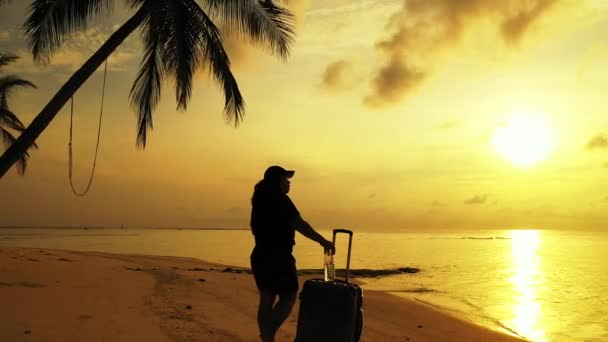 nő áll a trópusi strandon bőrönddel naplementekor - Felvétel, videó