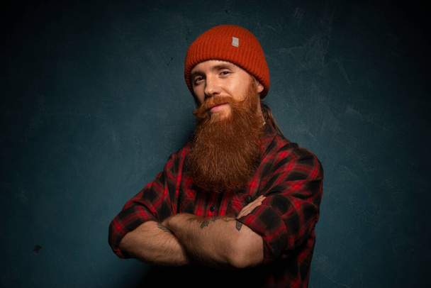 Red bearded man with orange hat and plaid shirt on the dark cyan background - Photo, Image