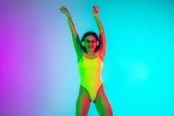 Schöne Mädchen in modischen Badeanzug isoliert auf Steigungen Studio Hintergrund in Neonlicht. Sommer, Resort, Mode und Wochenendkonzept - Foto, Bild
