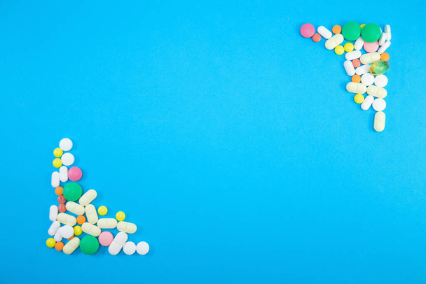 Group of colorful pills in left lower corner and right upper corner on blue background top view - Foto, afbeelding