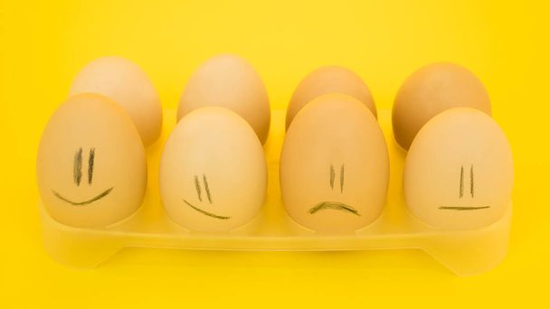 Chicken eggs in a tray with emotions on a yellow background. - Fotó, kép
