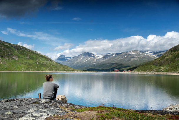Mujer joven viajero se sienta en un lago con montañas y colinas, viajando, hermoso paisaje del norte
 - Foto, Imagen