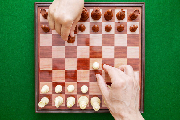 Image of hands playing chess on a green background. Hands start a chess game. World Chess Day. International Chess Day. July 20. View from above. - 写真・画像