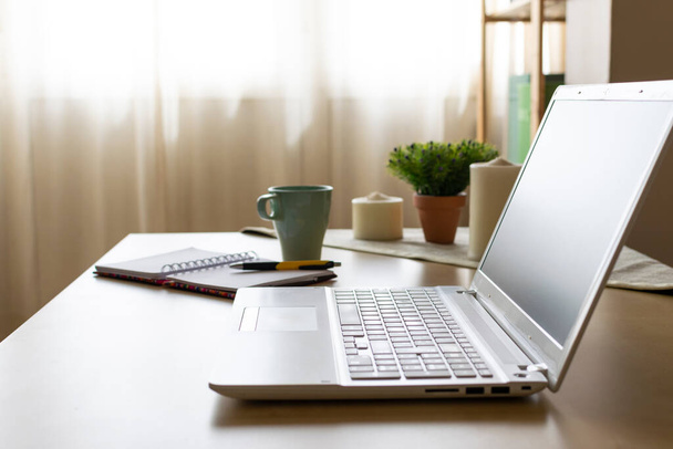 Kép egy barátságos környezetben egy otthoni irodai íróasztal laptop, papírok és egy csésze kávét és néhány gyertya a háttérben. Távközlő rezgések. - Fotó, kép
