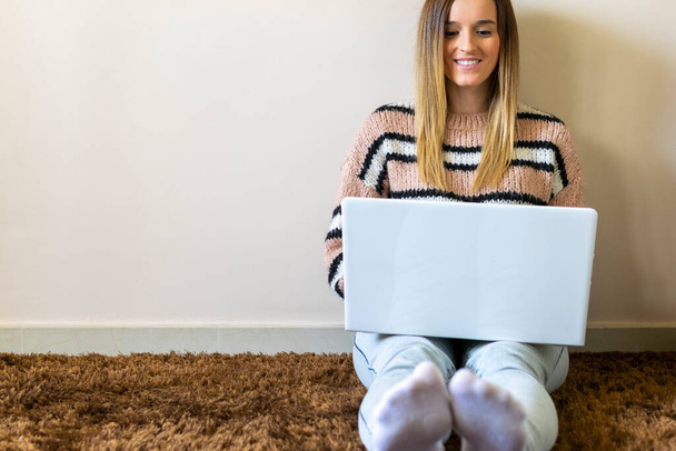 Feliz sorrindo caucasiano mulher atraente digitando computador portátil sentado no chão enquanto compras on-line e bate-papo. Fundo brilhante. Compras online
. - Foto, Imagem