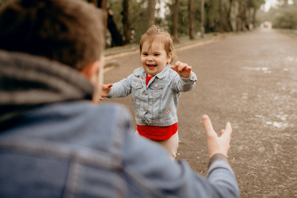 Isä ja tytär kävelevät sateessa puistossa, lapsen tunteet, märät vaatteet, lapsi juoksee isälle, tekstin paikka, perhe on pukeutunut farkkuihin, onnellinen lapsuus.
 - Valokuva, kuva