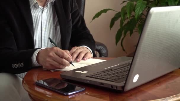 Empresario profesional inteligente que trabaja desde casa sentado frente a la computadora portátil tomando notas en una videollamada de conferencia teletrabajo
 - Metraje, vídeo