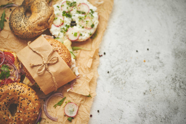 Bagels met ham, roomkaas, hummus, radijs verpakt in bruin bakpapier klaar om mee te nemen - Foto, afbeelding
