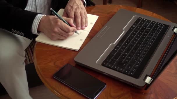 家から働いている専門家ビジネスマン彼のラップトップの前に座ってノートを取りますペンでノートを取りますビデオ会議コール - 映像、動画