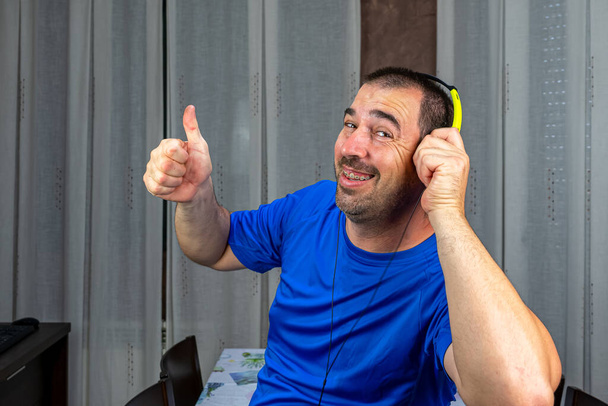 Homem barbudo com cabelo curto em camiseta azul e fones de ouvido móveis para ouvir música. Conceito de entretenimento
 - Foto, Imagem