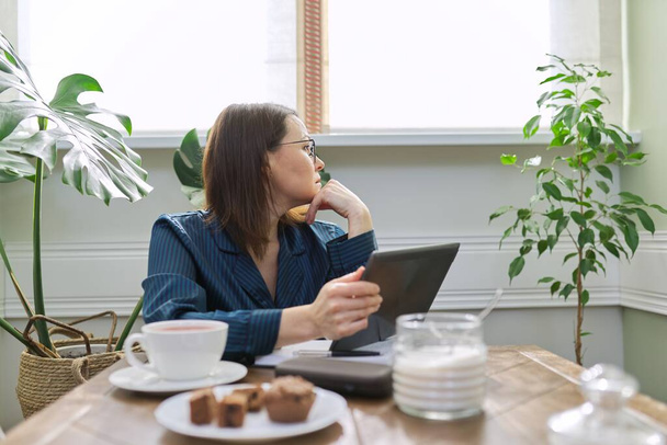 Serious mature woman working at home, using digital tablet, business notebook - Φωτογραφία, εικόνα