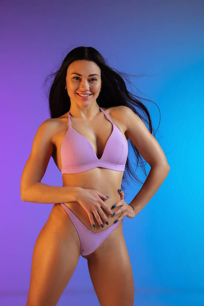 Fashion portrait of young fit and sportive woman in stylish purple luxury swimwear on gradient background. Perfect body ready for summertime. - Valokuva, kuva