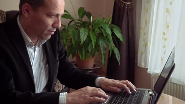 Intelligent senior adult male boomer internet surfing with his laptop with a plant on background - Video, Çekim