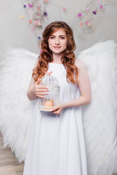 A young woman in a white dress with angel wings holds a cage in her hands. - Fotografie, Obrázek