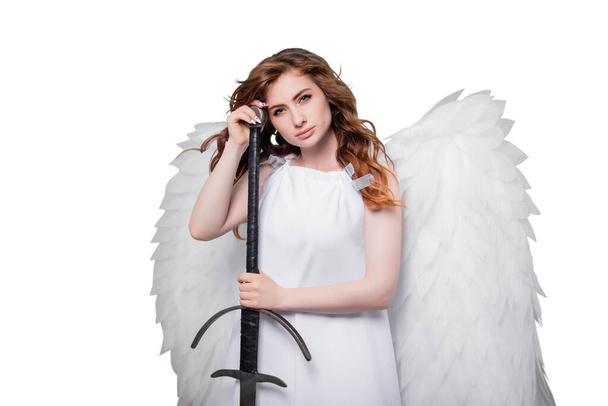 A young woman, an angel with wings in a white dress with flying hair posing with a sword in his hands isolated on a white background. - Photo, Image