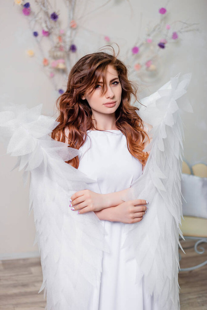 Πορτραίτο μιας νεαρής γυναίκας, ένας άγγελος με λευκό φόρεμα στέκεται τυλιγμένο σε φτερά. - Φωτογραφία, εικόνα