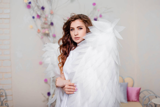 Πορτραίτο μιας νεαρής γυναίκας, ένας άγγελος με λευκό φόρεμα στέκεται τυλιγμένο σε φτερά. - Φωτογραφία, εικόνα